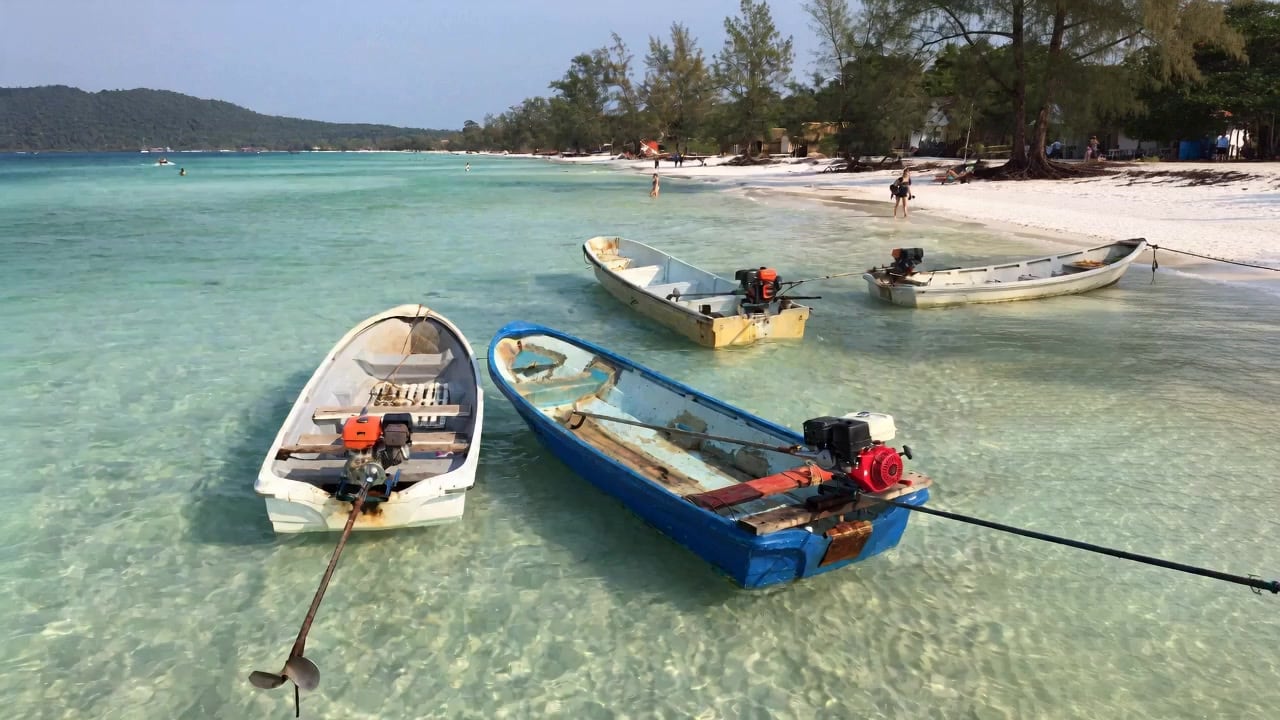 Local boats moored in clear turquoise shallows off a Koh Rong island beach