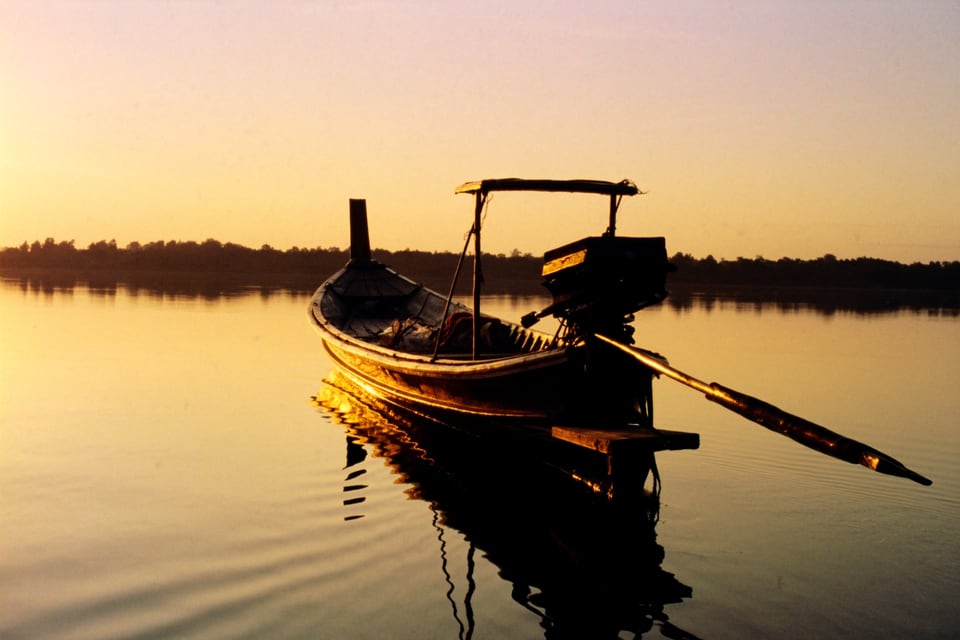 A Khmer long-tail boat on glassy water at sunset off the Cambodian coast